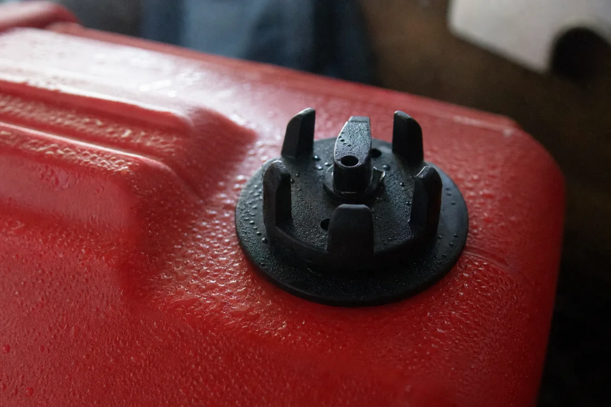The vent cap on a red portable fuel tank with condensation beaded around it.