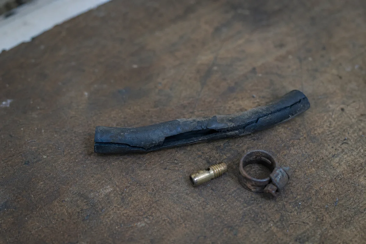 An old outboard fuel line gone soft and cracked, beside a carburettor jet and a rusty clamp.