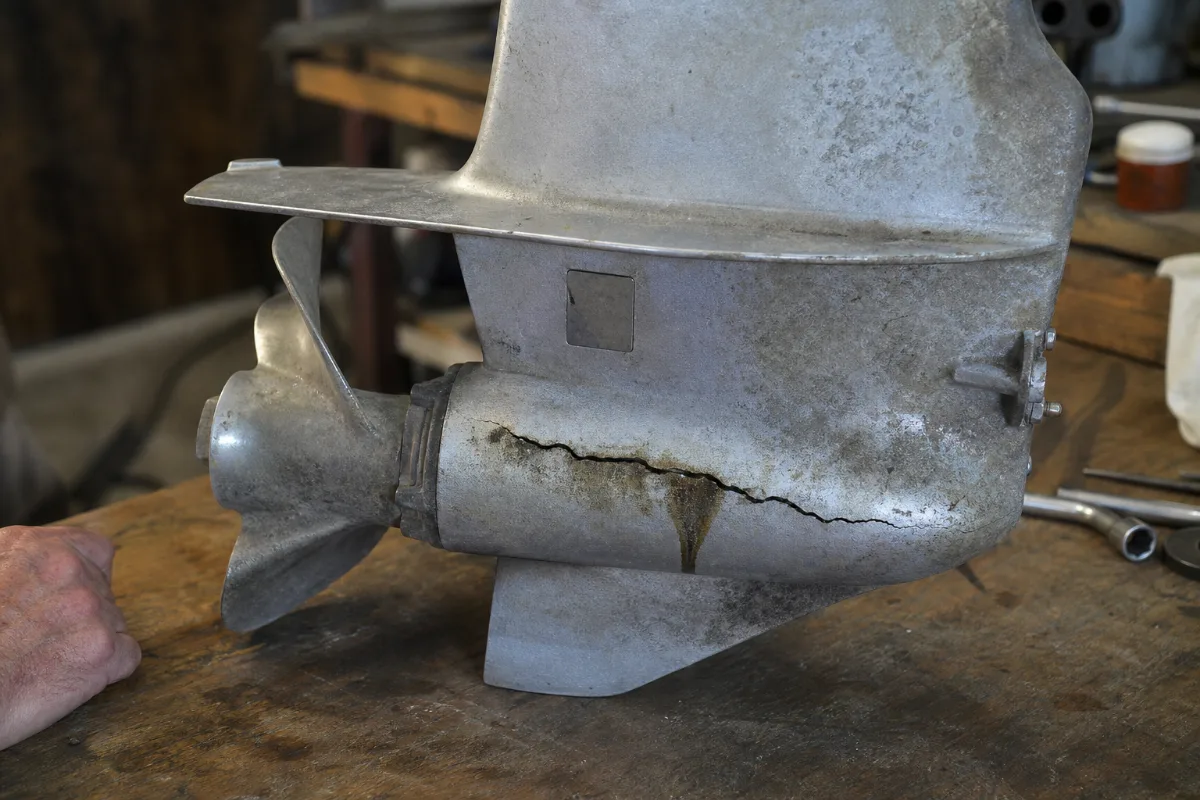 A cracked aluminum gearcase on an old outboard lower unit, stained with gear oil around the crack.