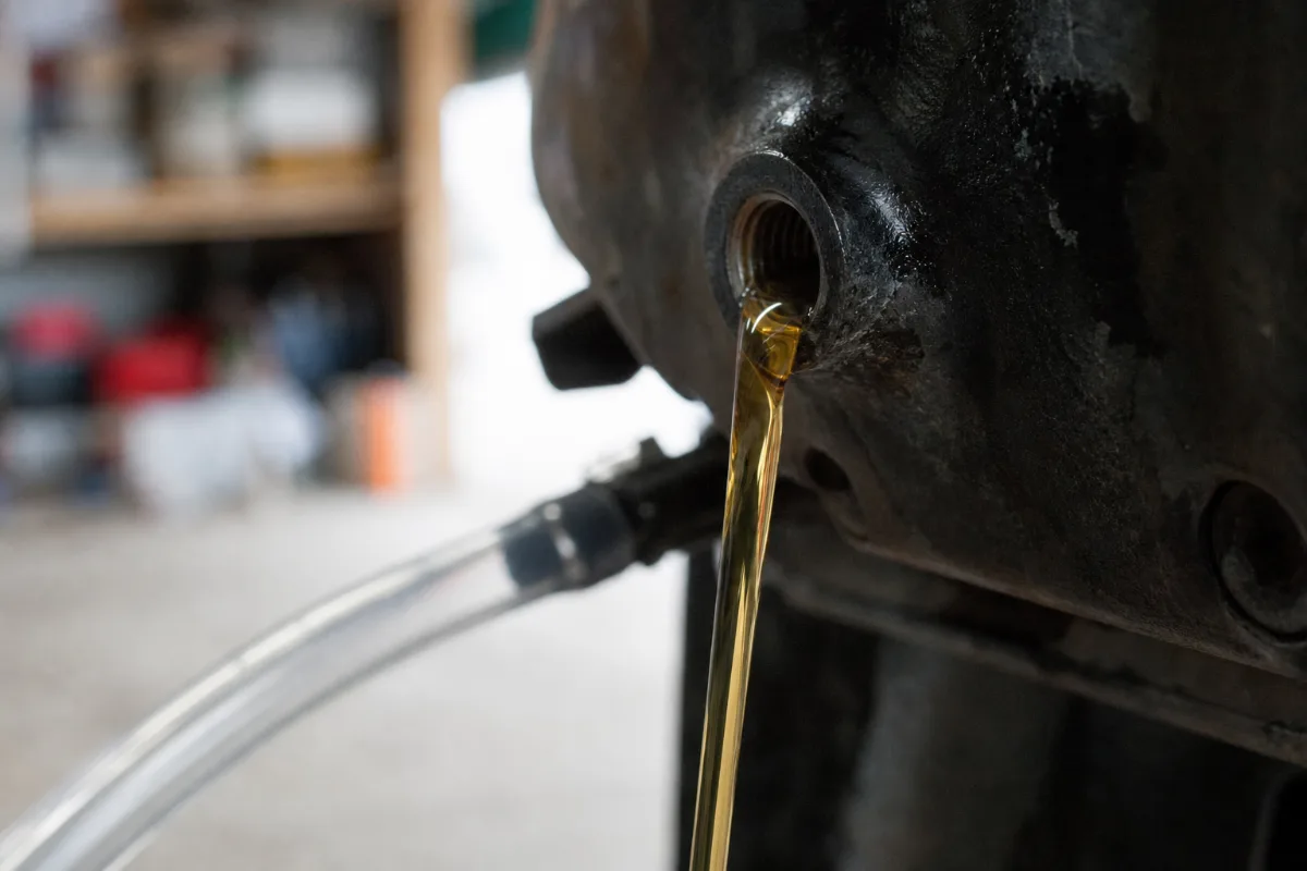 Fresh gear oil flowing out of the top vent hole of an outboard gearcase as it is filled from the bottom.