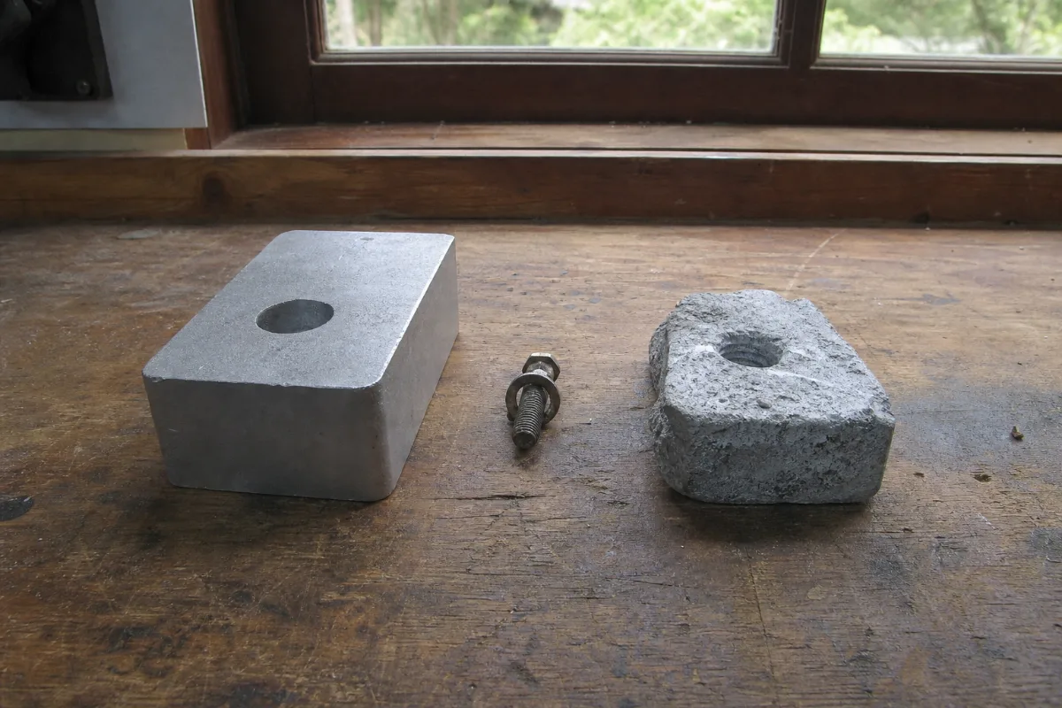 A new anode block beside one eroded to about half its original size on a workbench.