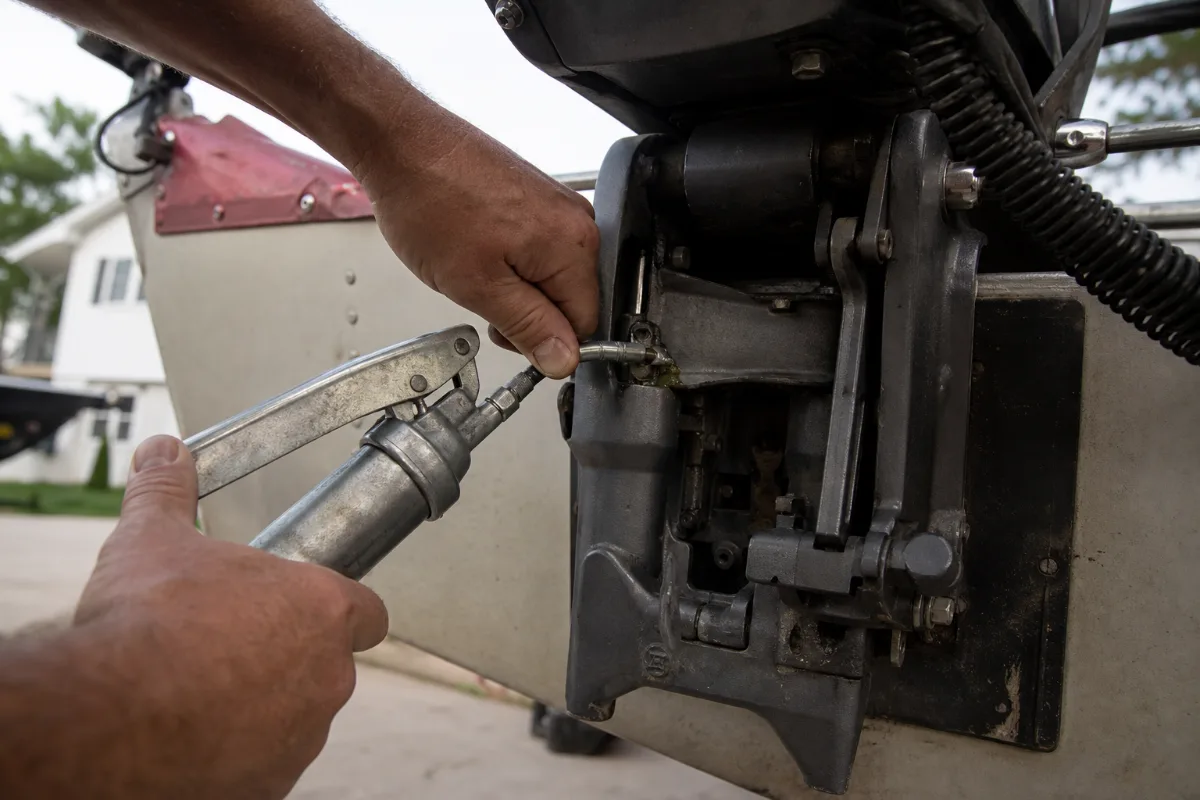 Fresh marine grease being pumped into the swivel bracket grease fitting on an outboard motor.