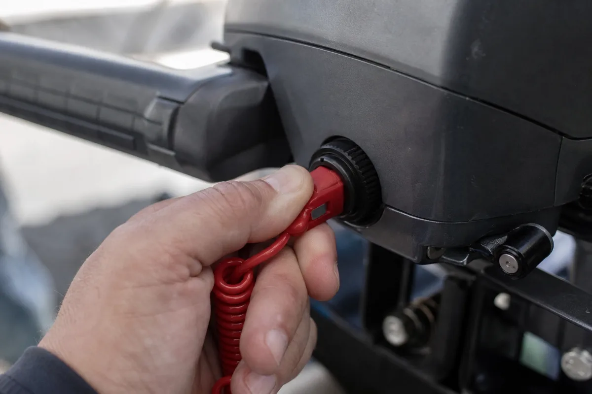 A red kill switch lanyard clip being pushed into the safety switch on an outboard tiller.