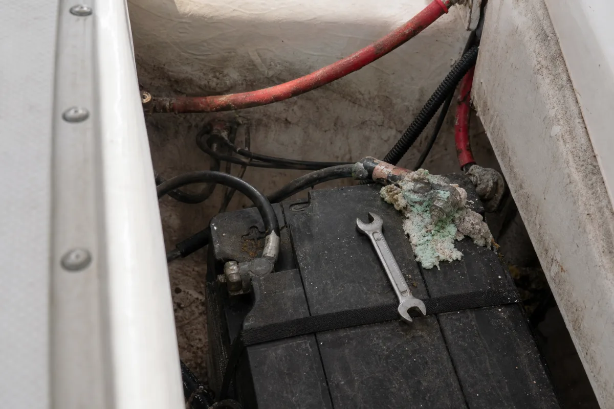 A corroded battery terminal with white and green crust on a marine battery in a boat locker.