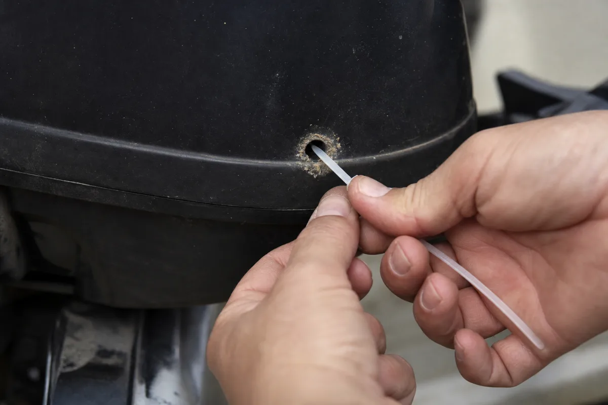 A zip tie being pushed into the small tell-tale outlet hole on an outboard to clear a clog.