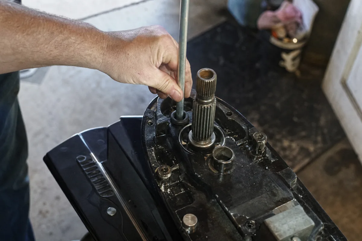 A hand guiding the metal water tube into the rubber grommet on top of an outboard water pump housing.