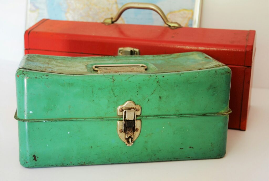 Two old metal boxes with latches and handles, a green one in front of a red one