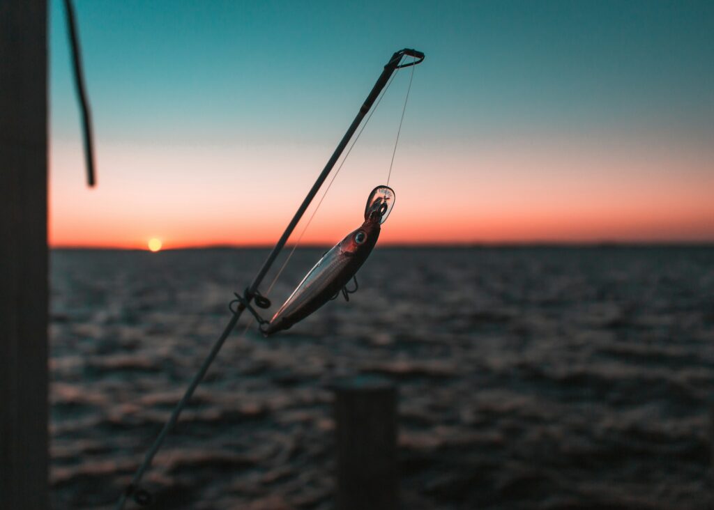A minnow-shaped crankbait hanging from a rod near a dock post at sunset over the water