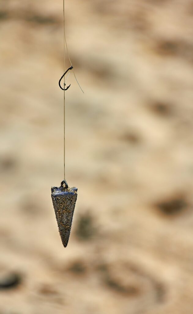 A single hook and a pyramid sinker hanging on fishing line over sand