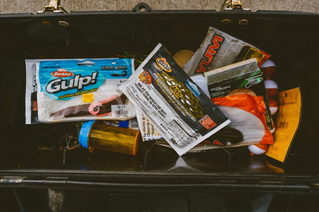 Packs of soft plastic baits still in their bags, piled in an open black tackle box