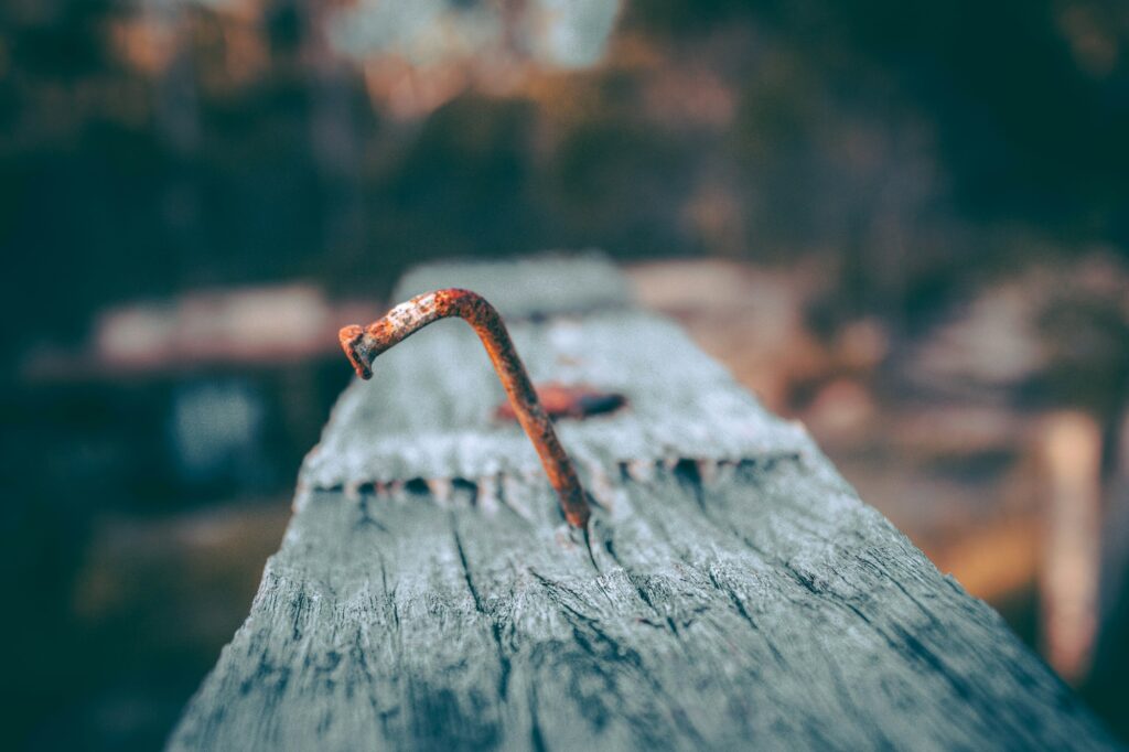 A bent, rusted nail sticking out of a weathered dock board