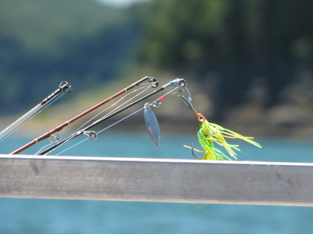 A chartreuse spinnerbait hanging from fishing rod tips over a rail by a lake