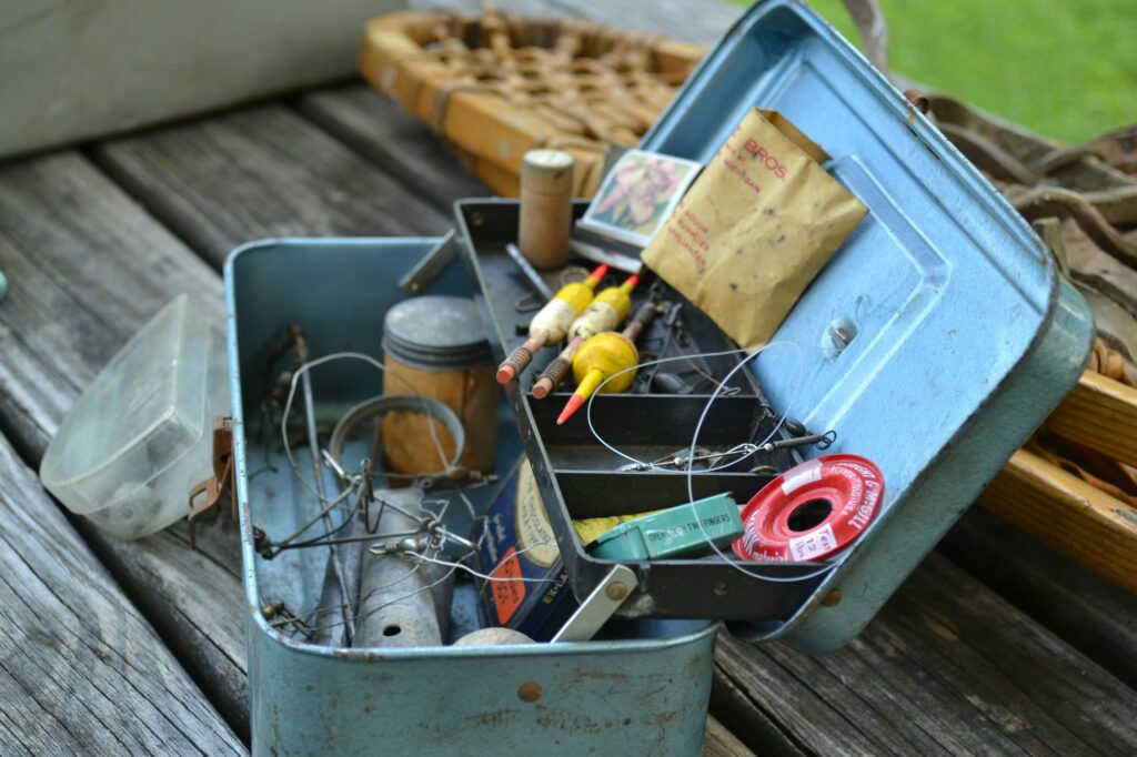 An open blue metal tackle box crammed with floats, a spool of line, hooks and loose packets on a wooden table