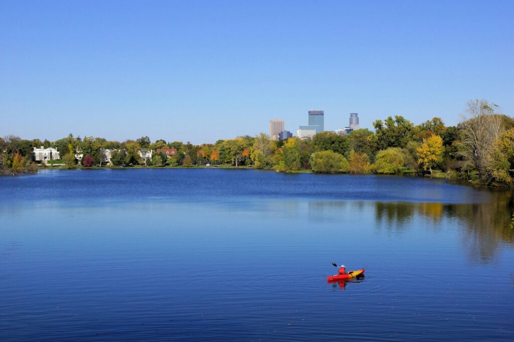 A paddler in a red kayak alone on a big open lake ringed by fall trees