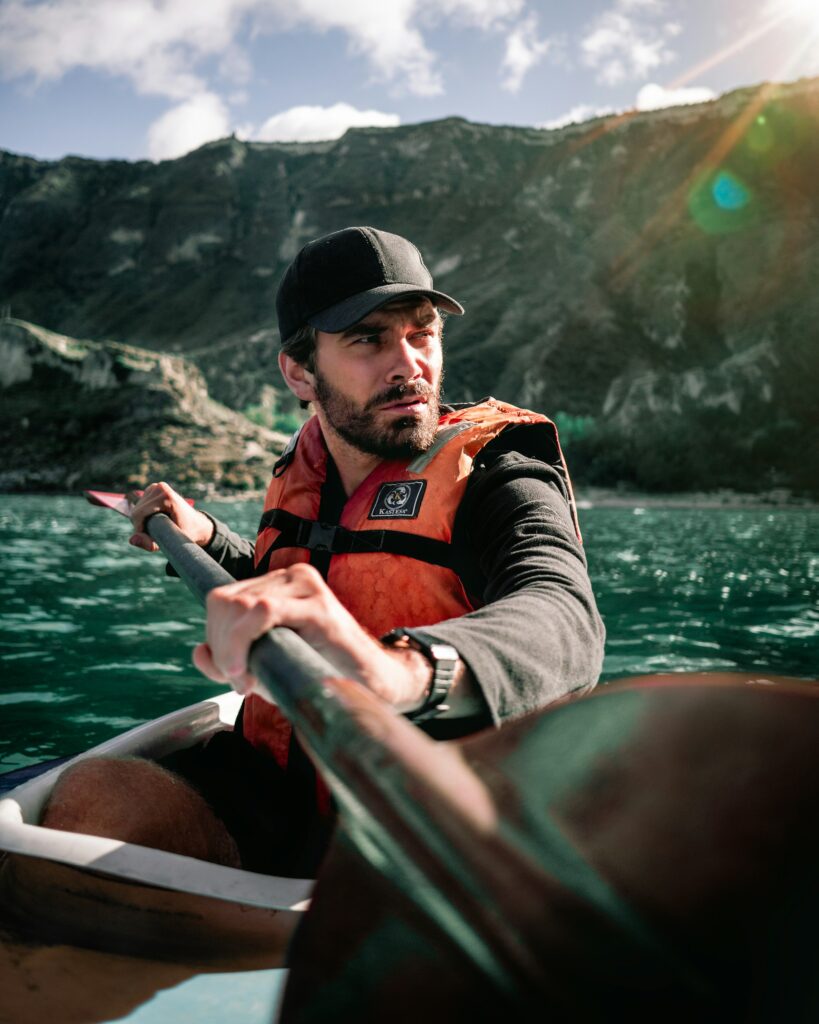 A man paddling a kayak in an orange life jacket and a cap